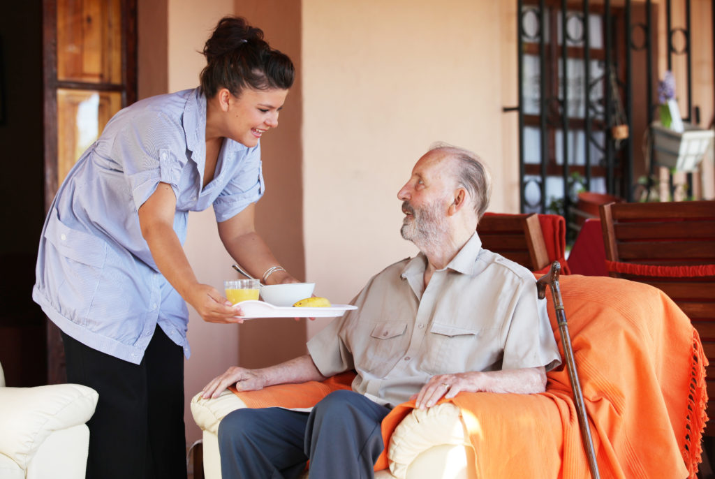 un soignant apporte un repas à une personne âgée